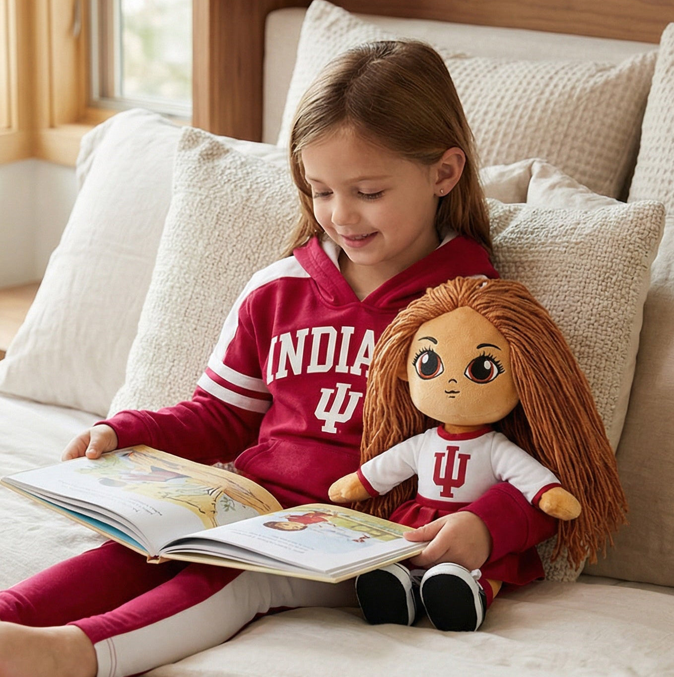 Young girl in a red Indiana University sweatshirt reading a book to a doll on a bed.
