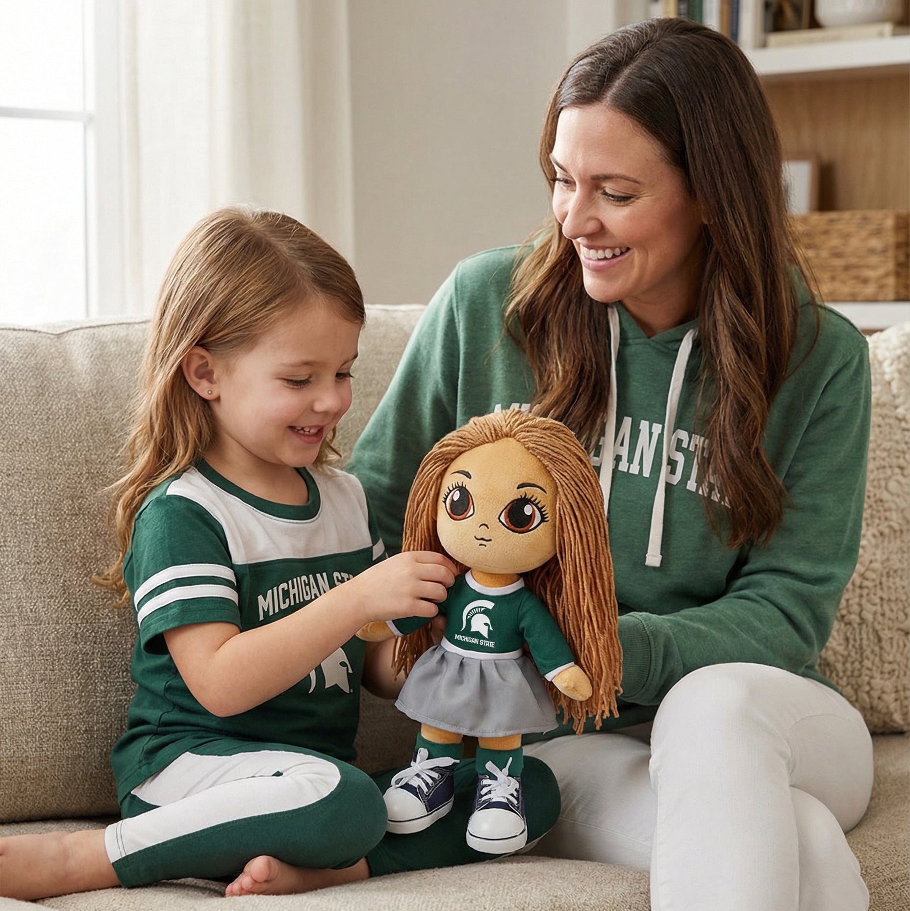 Woman and child sitting on a couch with a doll wearing a Michigan State uniform.