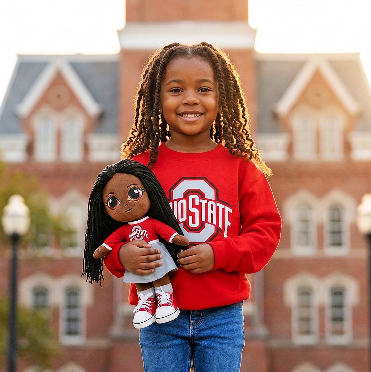 Child holding a doll in front of a brick building
